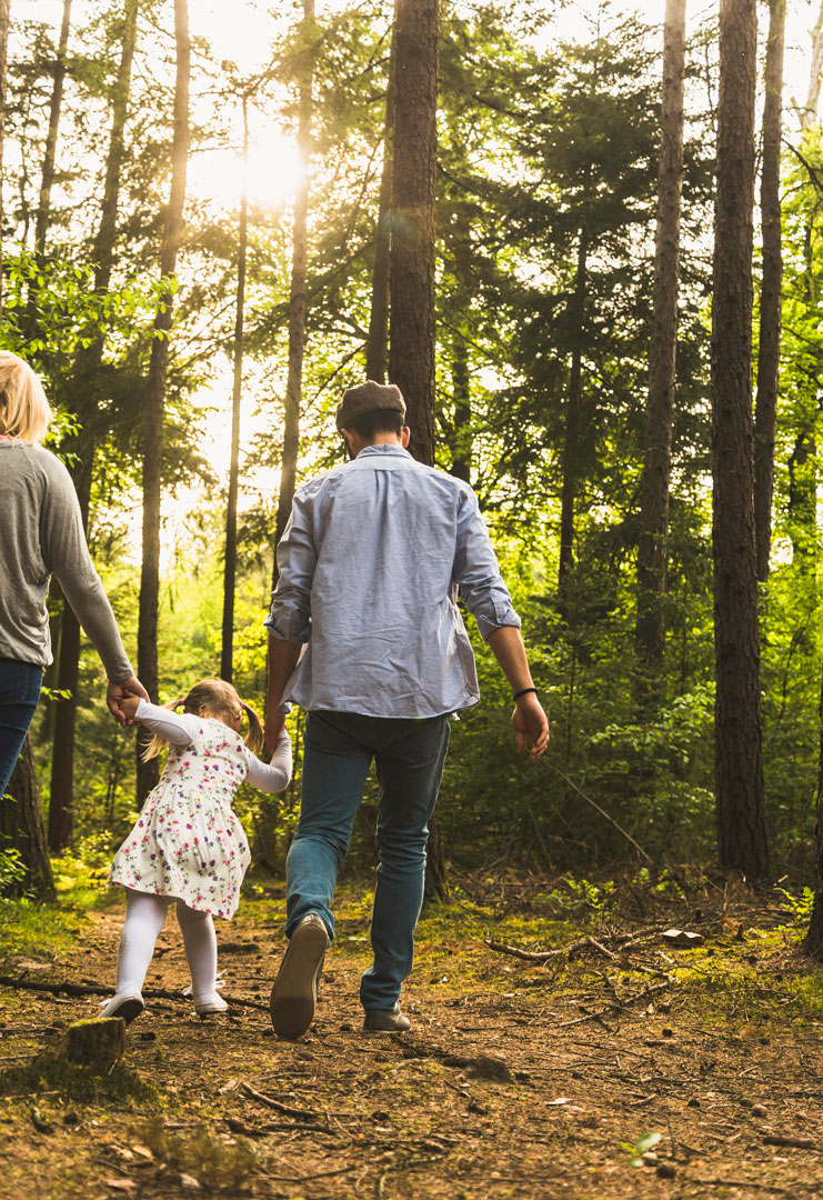 Family walking hand-in-hand through a sunlit forest trail with young child