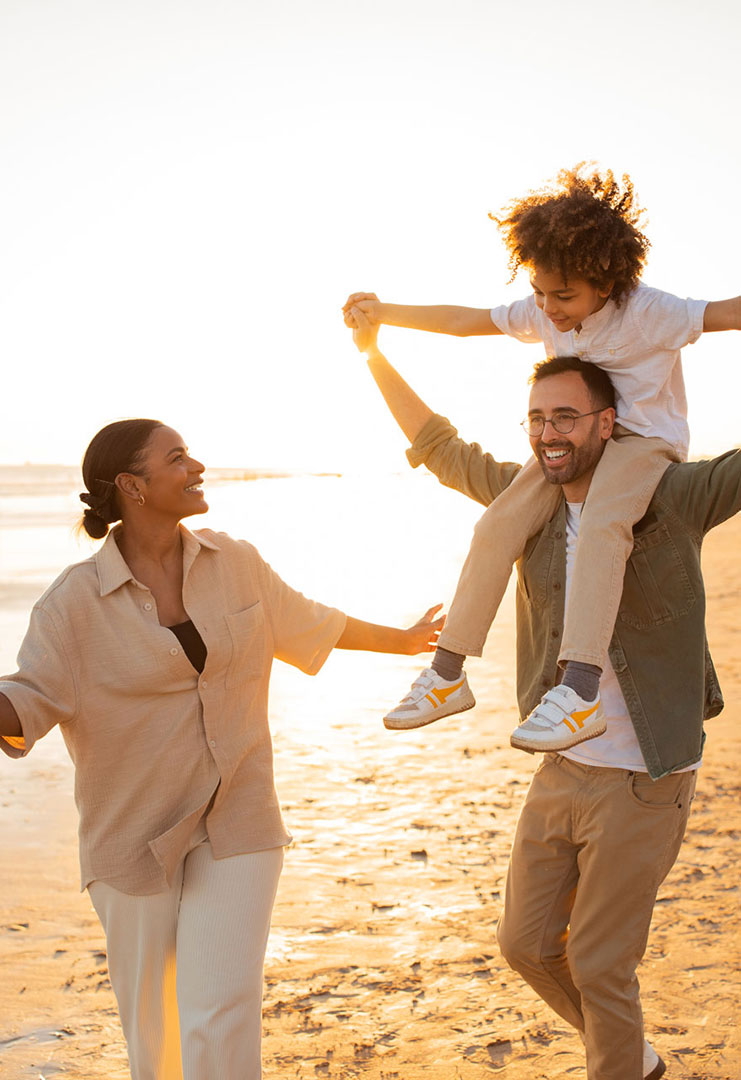 Smiling family walking along the beach at sunset with child on shoulders